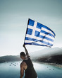 © Cavan Images - Rear view of man waving Greek flag while standing over sea against sky