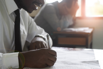 African man writing and reading exam answer sheets exercises in classroom of school with smile