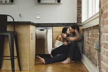 Smiling Couple Sitting By Wall In Kitchen At Home