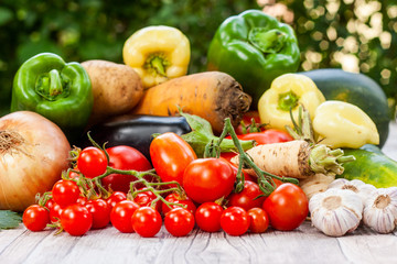 Colourful variety of fresh home grown vegetables from an organic garden on a wooden surface. Tomato, green and yellow bell peppers, carrot, parsley, onion, garlic, potato, eggplant and zucchini.