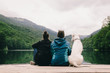 © minastefanovic - Couple sitting with a dog on dock at the lake. Back view