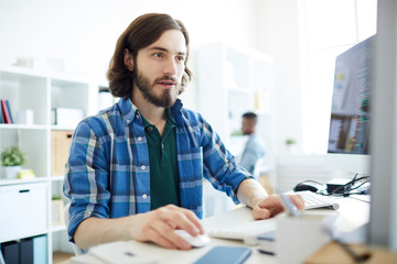 Wall Mural - Young handsome man in casualwear working with database while sitting in front of computer monitor