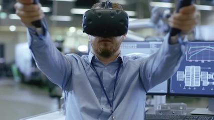 Fototapete - Portrait Shot of the Industrial Engineer Wearing Virtual Reality Headset and Using Controllers, ready to Work. In the Background Manufacturing Plant and Monitors.