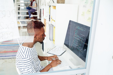 Wall Mural - African-american it-specialist looking attentively at coded data on computer screen while working in office