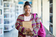 © pressmaster - Positive confident overweight African-American student girl in colorful cardigan holding sketchpad and smiling at camera in library