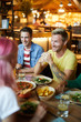© pressmaster - Two happy guys in casualwear talking to girls while sitting by table and having dinner in cafe