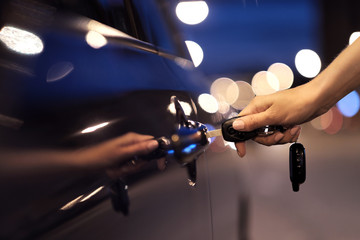 Close-up of a female hand pressing a button on a key ring of car keys, against the background of a car door.