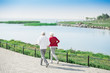 © Seventyfour - Back view portrait of active senior couple running together in park along lake, copy space