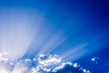 Sunbeams rising from a large cloud in intense blue sky on a summer afternoon