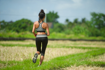 back view of young runner woman with attractive and fit body in running outdoors workout at beautiful off road track green landscape background