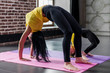 © undrey - Woman and child girl practicing yoga together at home, standing in bridge pose