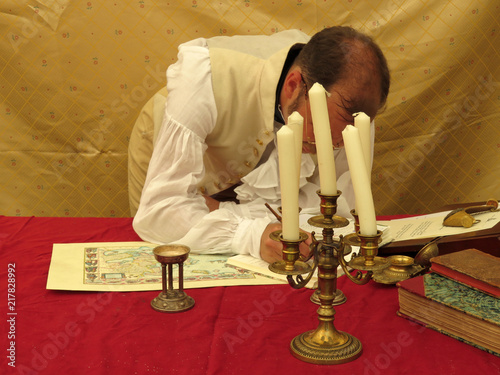 Photographie Man in clothes of the 19th century writes with a ink pen at a table with maps and books