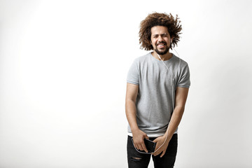 Wall Mural - A curly-headed handsome man wearing a gray T-shirt is standing with a joyous smile and listening to music in the earphones over the white background.