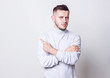 © oleg_ermak - Portrait of rowned casual man wearing a white turtleneck shirt with his arms crossed over his chest pointing finger to side while standing on grey background copy space