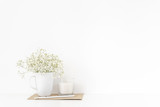 Fototapeta Kwiaty - Background with stationary, white candle, pencil and bouquet of white flowers in mug on white wall background, summer home decor. Copy space for text. Empty space for lettering.