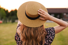 Portrait From Back Of European Woman 20s Wearing Straw Hat And Dress, Walking Outdoor On Nature In Countryside