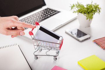 Bank card nearby a laptop and mini shopping cart