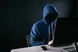 Anonymous and faceless hacker under hoodie using computer isolated over dark background - illegal online internet criminal concept.