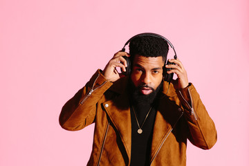 Wall Mural - Stylish, handsome and cool African American man with beard, listening to music, isolated on pink studio background
