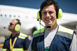 Having good time at work. Cheerful man looking at camera with smile. Colleague and passenger plane on blurred background