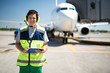 Doing job with joy. Cheerful man posing at airdrome. Passenger plane on blurred background
