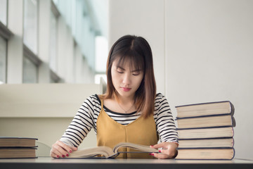 Wall Mural - smart woman college student reading books; portrait of focused woman university student studying, researching, reading book in library; asian young adult woman mode