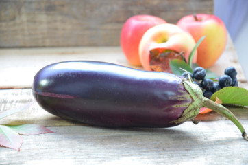 Harvest - ripe juicy eggplant (aubergine). Eggplants with autumn fall leaves and apples. The t aubergine lies on a wooden kitchen background. copy space