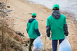 © pressmaster - Back view of unrecognizable activists in green uniform walking to polluted shore with garbage bags