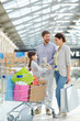© pressmaster - Happy parents carrying shopping cart with girl and paper bags in shopping mall enjoying weekend