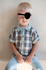 happy blond child with black medical patch occluder on eye