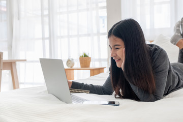 Poster - Asian woman laying on bed doing paperwork on laptop in bedroom.work at home.e-larning concept.study online.