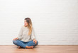 © Krakenimages.com - Young adult woman sitting on the floor over white brick wall at home looking away to side with smile on face, natural expression. Laughing confident.