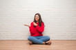 © Krakenimages.com - Young brunette woman sitting on the floor over white brick wall very happy pointing with hand and finger