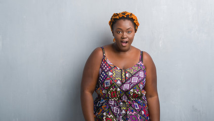 Canvas Print - Young african american woman over grey grunge wall wearing orange braids afraid and shocked with surprise expression, fear and excited face.