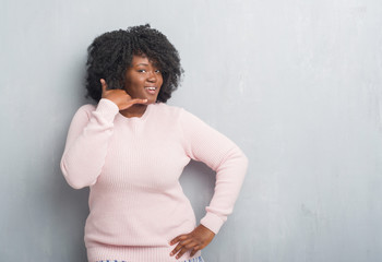 Canvas Print - Young african american plus size woman over grey grunge wall wearing winter sweater smiling doing phone gesture with hand and fingers like talking on the telephone. Communicating concepts.