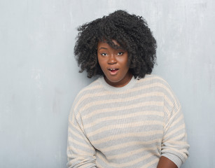 Canvas Print - Young african american plus size woman over grey grunge wall wearing a sweater afraid and shocked with surprise expression, fear and excited face.