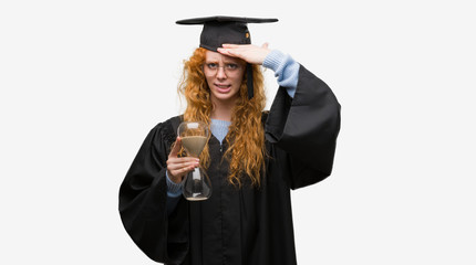 Sticker - Young redhead student woman wearing graduated uniform holding hourglass stressed with hand on head, shocked with shame and surprise face, angry and frustrated. Fear and upset for mistake.