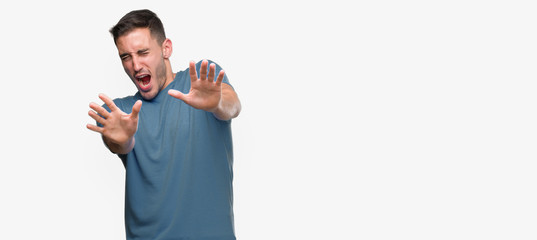 Canvas Print - Handsome young casual man afraid and terrified with fear expression stop gesture with hands, shouting in shock. Panic concept.