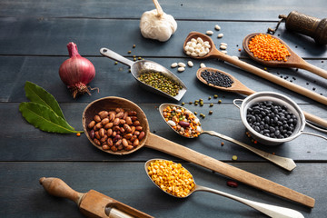 Canvas Print - Top view of flat lay of assortment of legumes pulses on black wooden tabletop background, in scoop and ladles and grater.