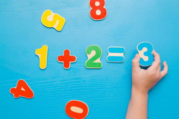 Colorful learning numbers for little kids on the blue table. Girl's hand putting number three. Right answer. Time to learn. Education concept. Top view.