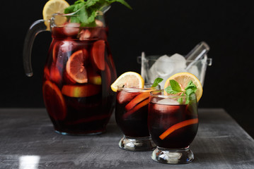 Refreshing sangria or punch with fruits in glasses and pitcher. Red sangria with strawberry, mint leaves, ice. Cocktail bar. Selective focus.