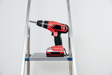 Poster - The screwdriver is located on the ladder. The concept of renovation, removal and planned changes in the apartment. A red cordless is on a light background.