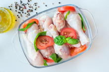 Raw Uncooked Chicken Legs, Drumsticks With Tomatoes And Basil In A Glass Backing Dish, Meat With Ingredients For Cooking, Horizontal, Top View