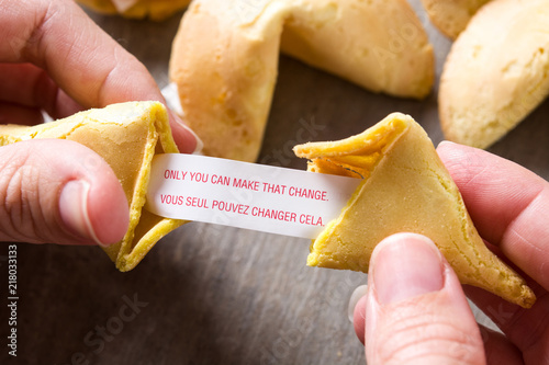 Fotografía Hand opening fortune cookie with message on paper on wooden table