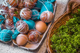 Fototapeta  - Easter eggs prepared for dyeing in onions peels, decorated with natural fresh leaves, plants, rice, colorful fabric and tied with white threads. Eggs laying in wicker wooden basket full of green grass