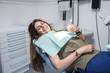 © pablobenii - Portrait of a blue-eyed young woman sitting in the chair of a dental clinic gesturing thumb up