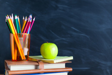 Back to School cocept. Still life with school books, pencils and apple against blackboard background