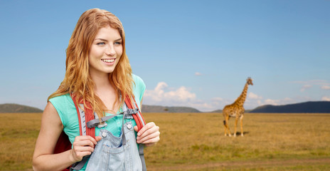 Wall Mural - adventure, travel, tourism, hike and people concept - smiling young woman with backpack over giraffe in african savannah background