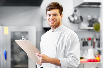 Wall Mural - cooking, profession and people concept - happy smiling male chef cook writing to clipboard and doing inventory at restaurant kitchen