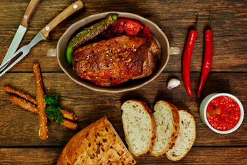 Wall Mural - Baked pork loin  in ceramic form with fork, knife and homemade rustic bread on dark rustic background. Roasted pork served with grilled vegetables and tomato sauce. Cozy village dinner..